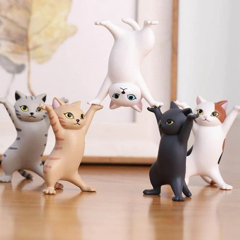 Five dancing cat figurines, 4 of them are on a wooden table and the 5th one is upside down being held by 2 of the other figurines.