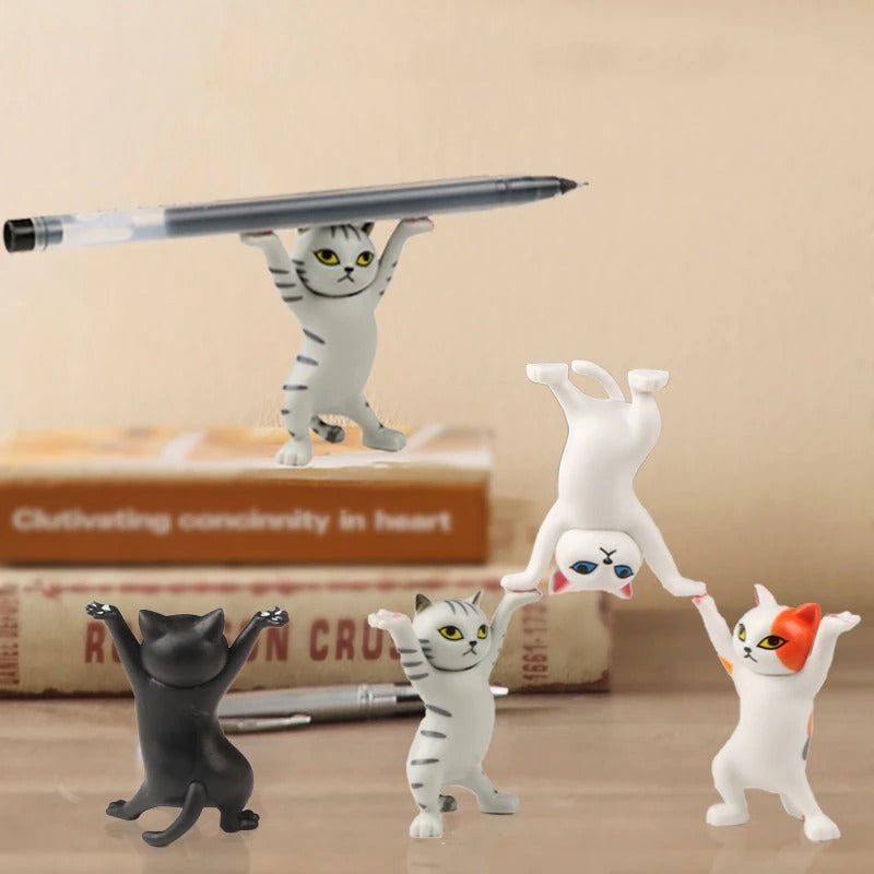 Five dancing cat figures on a wooden table, one of them is in the background on top of two books and is holding a pen.