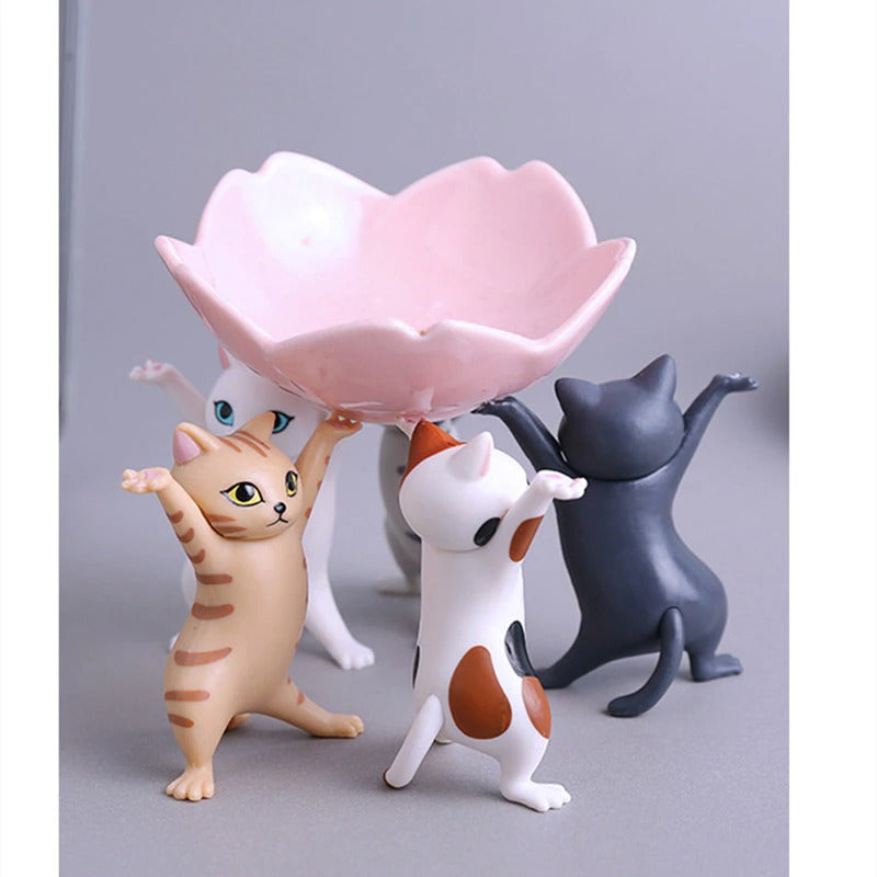 Five dancing cat figurines holding up a small pink bowl.