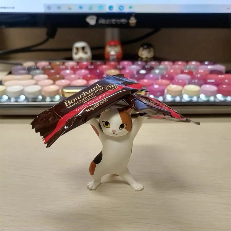 A dancing cat figurine holding up two small bars of chocolate.