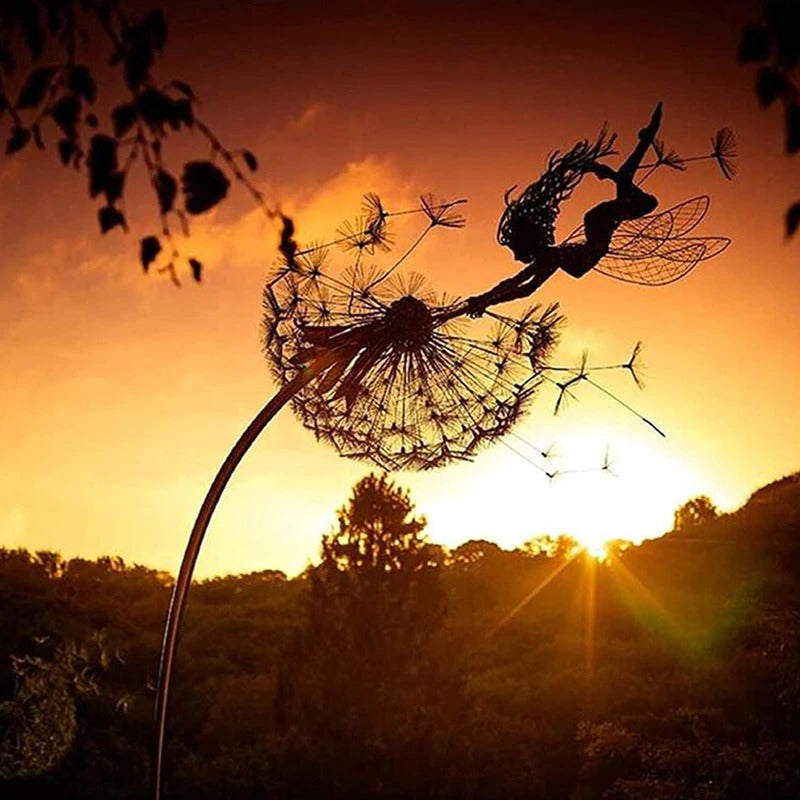 A fairy metal sculpture in a garden with a setting sun behind it. The setting sun outlines the metal sculpture and makes it look like a fairy is swinging around a dandelion as pieces of the dandelion are falling away.