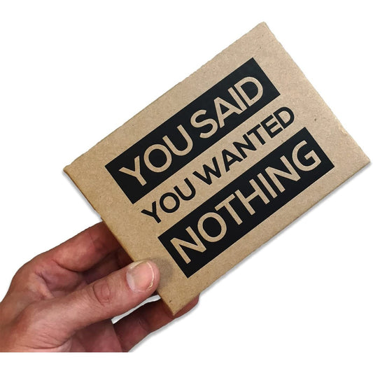 A hand is holding a brown box which has large bold text on the lid which says, 'You said you wanted nothing.'
