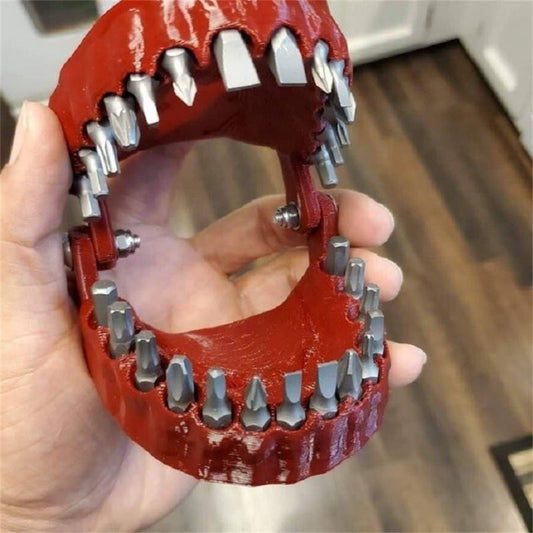 A red colored drill bit holder which is in the shape of a human upper and lower jaw. Drill bits can be held in place of the teeth.