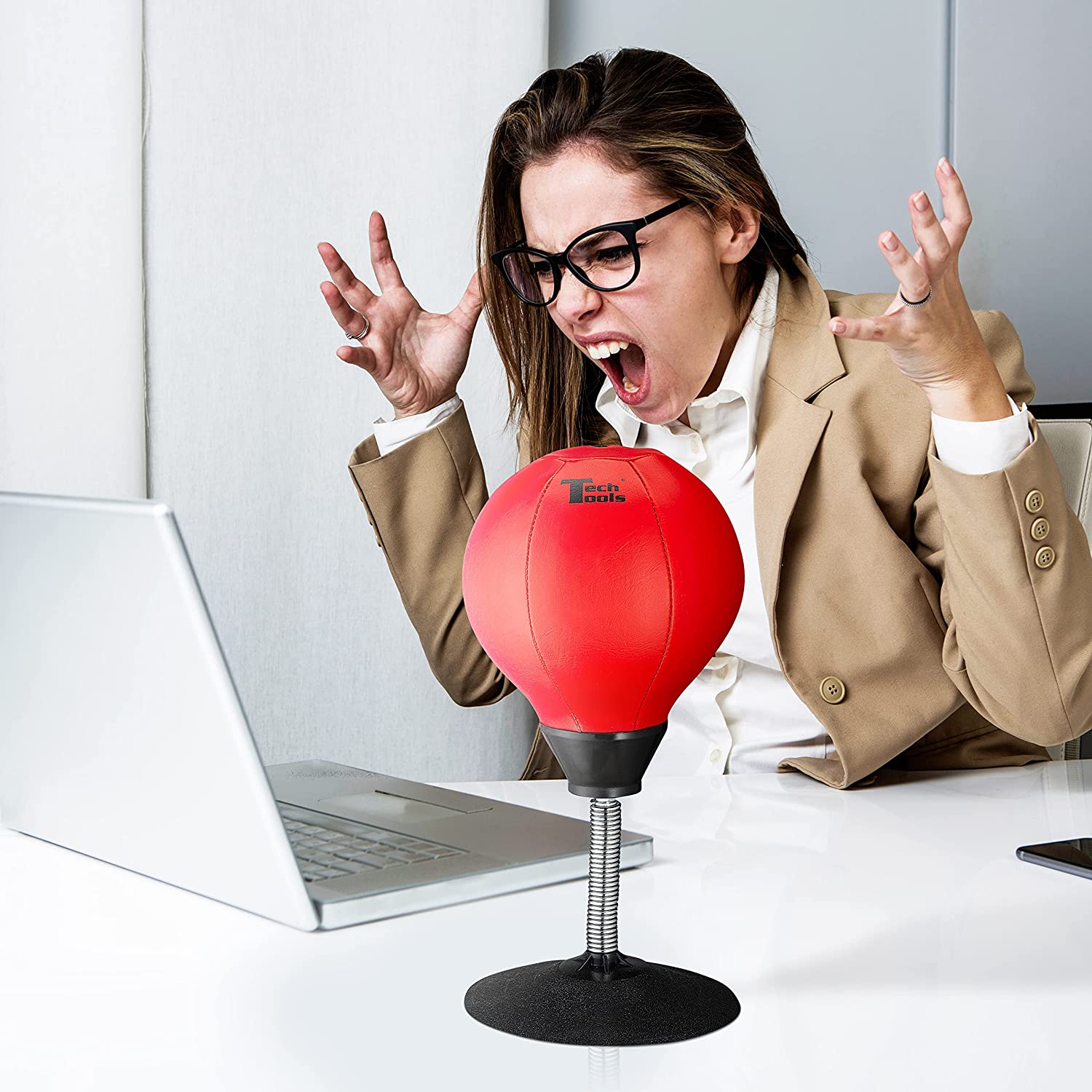 An angry woman in front of a laptop has a desktop punching bag next to her.