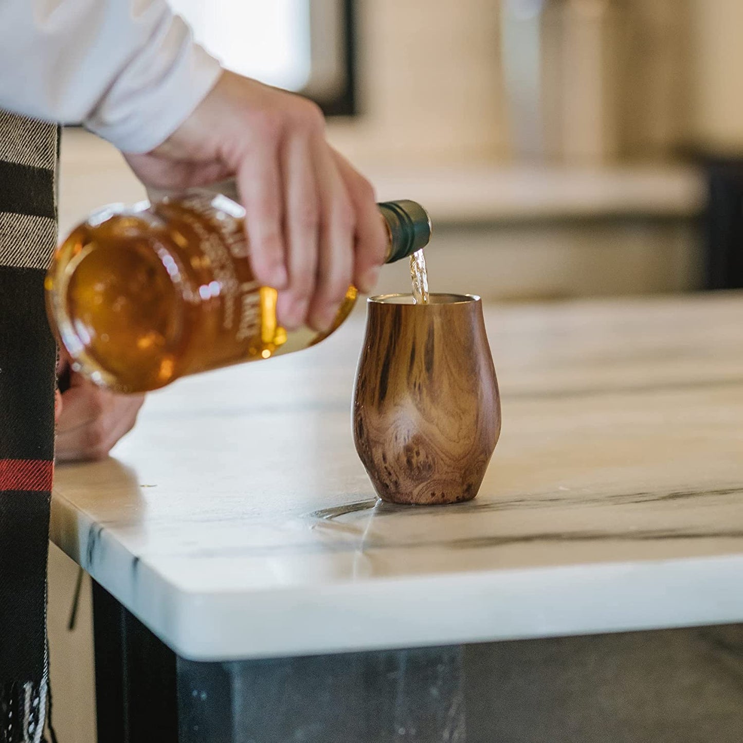 A hand is pouring some whiskey into a whiskey nosing glass.