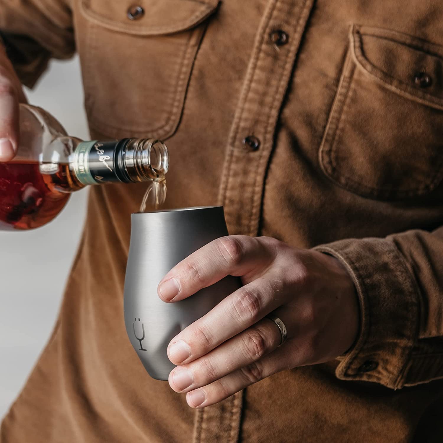 A man is pouring some whiskey into a whiskey nosing glass.