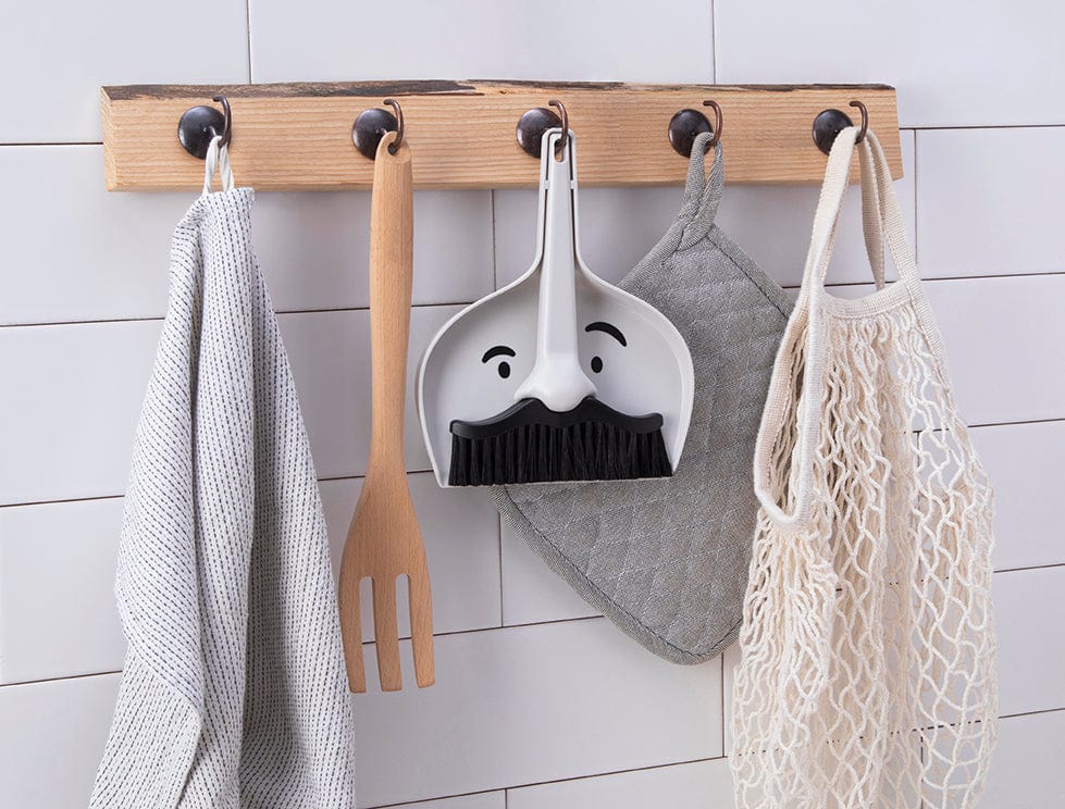 A dustpan and brush set with eyes printed on the dustpan and the broom as a moustache hanging on a wall