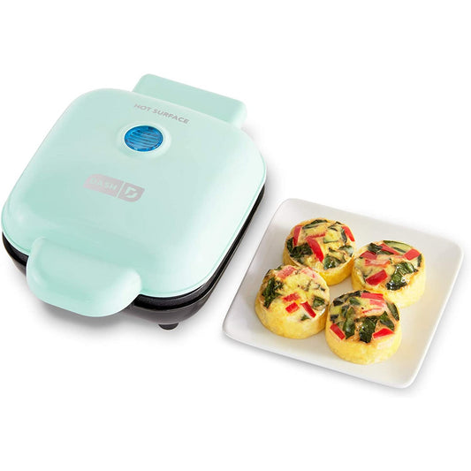 An aqua colored egg bite and sandwich maker with a plate of 4 cooked egg bites on a plate next to the cooker.
