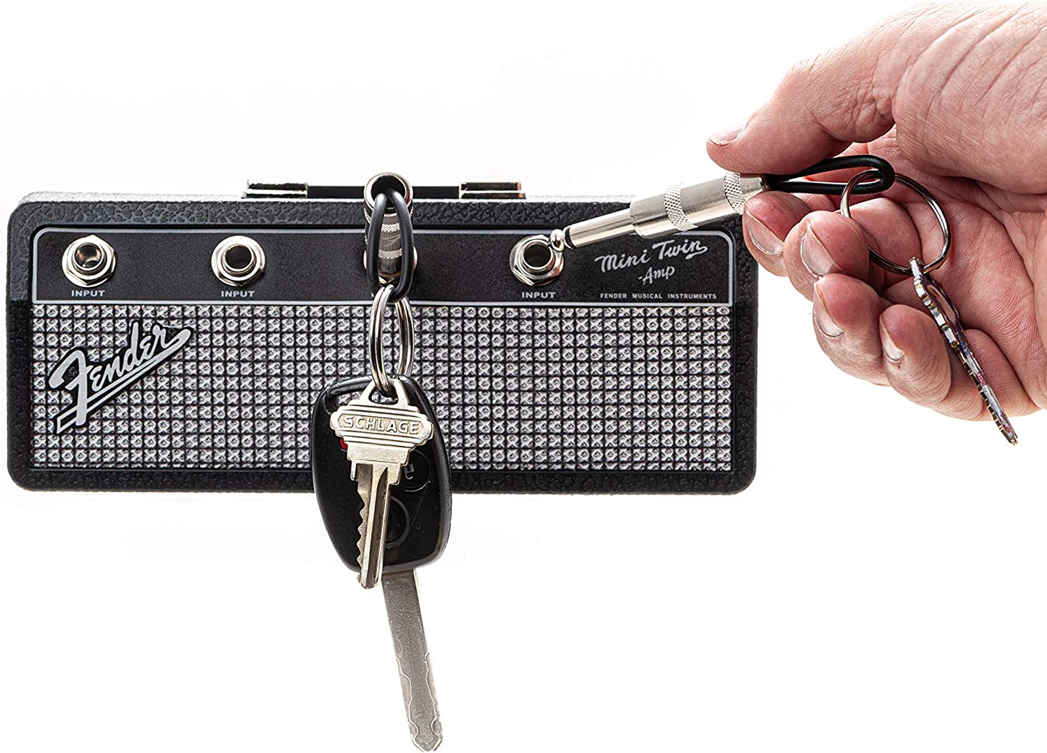 A Fender jack key holder rack with a hand putting a keychain into one of the plugs and a set of keys hanging from one of the other jacks.