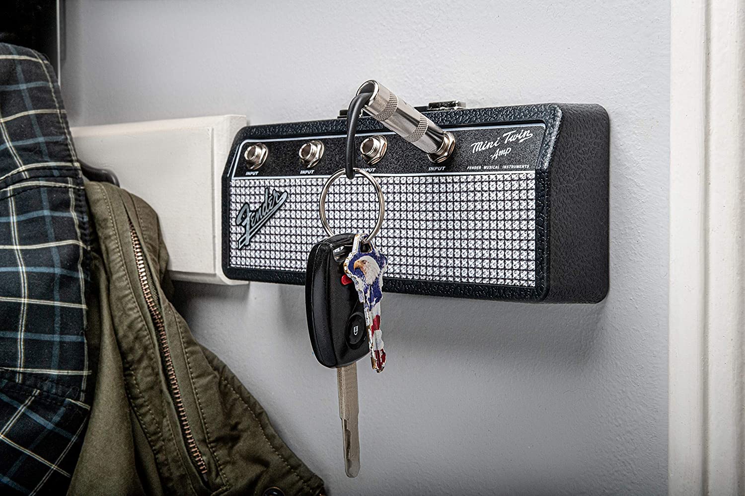 A Fender jack rack key holder on a white wall with a guitar plug keychain hanging from one of the plugs with keys on it. 