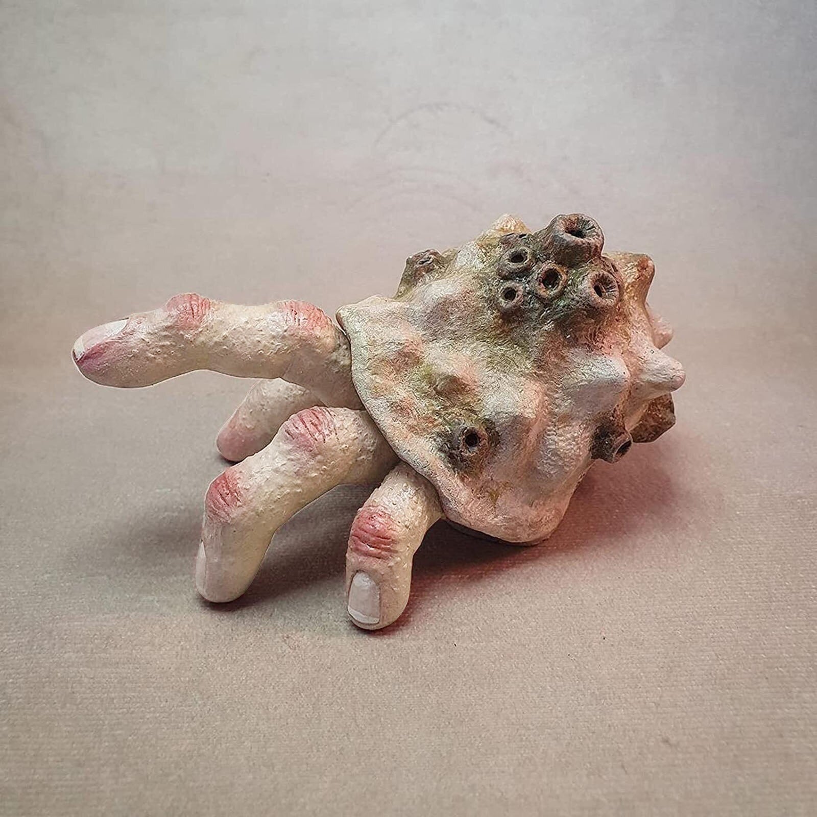 A hermit crab finger sculpture which has 6 fingers and appears to be walking with one finger in the air.