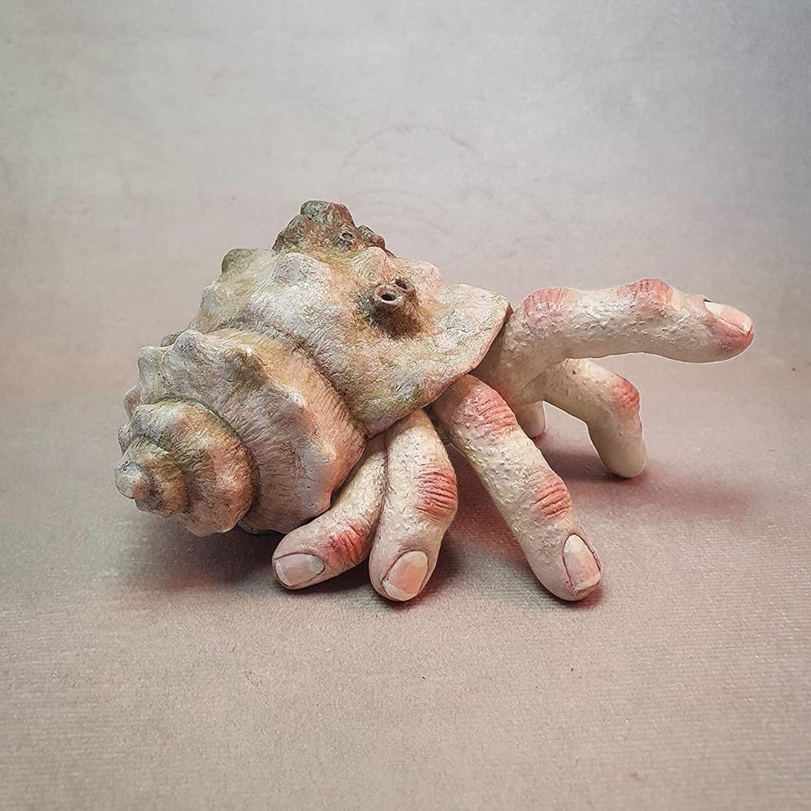 A hermit crab finger sculpture which has 6 fingers and appears to be walking along a surface with one finger in the air.