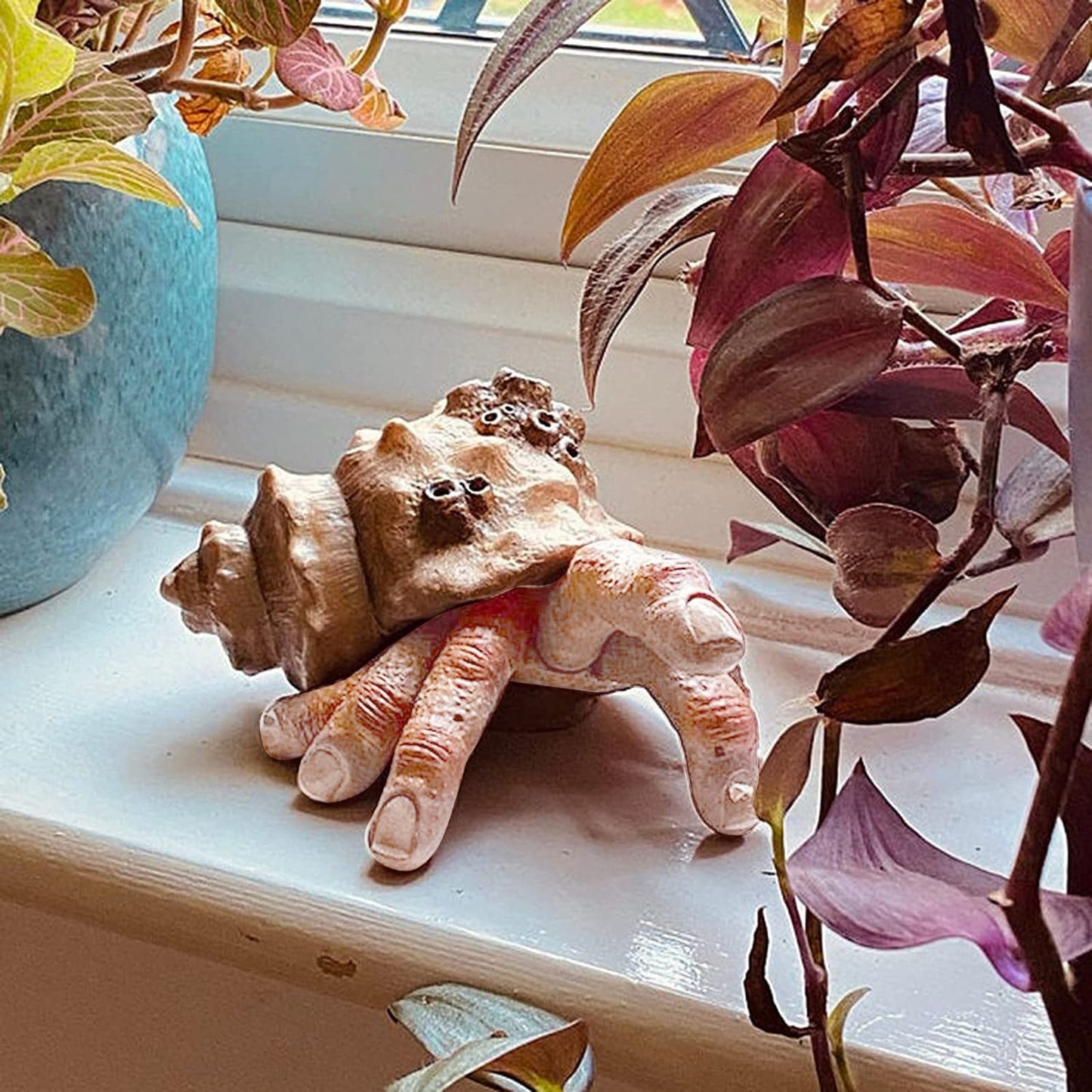 A hermit crab finger sculpture on a window sill. The sculpture has 6 fingers and appears to be walking along the window sill with one finger in the air.
