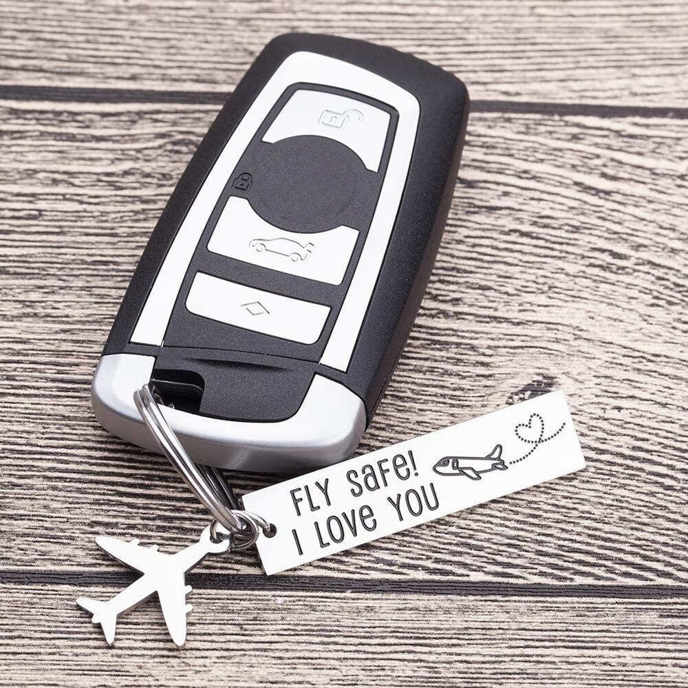 A silver keychain is attached to a car remote. The keychain has a tag which reads fly safe, I love you and also has a silver airplane hanging off it too.