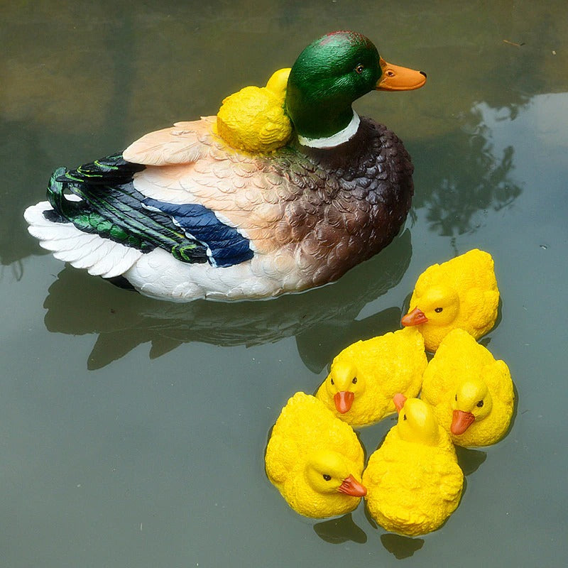 A decorative mother duck and five ducklings all made from resin floating in a pond.