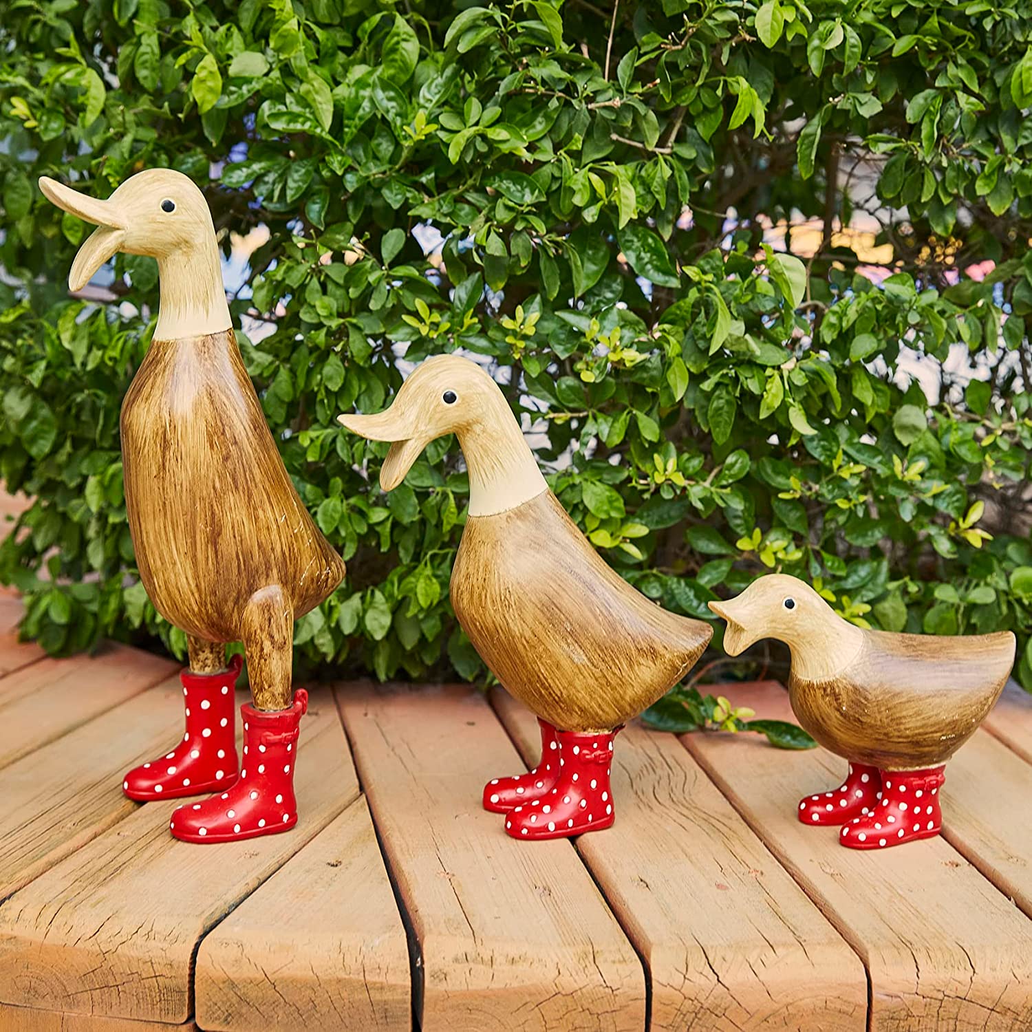 Three wooden garden decor ducks in different poses. All three ducks are wearing red, spotted wellington boots.