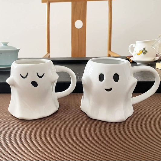 Two cute white ghost shaped coffee mugs with happy expressions.