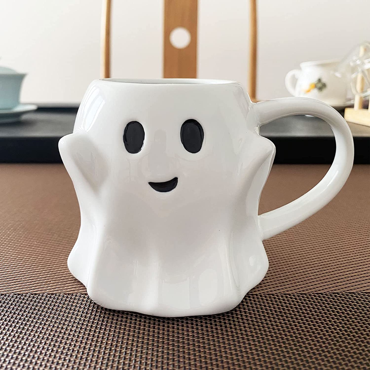 An adorable white ghost shaped ceramic coffee mug with a happy expression printed on the outside.