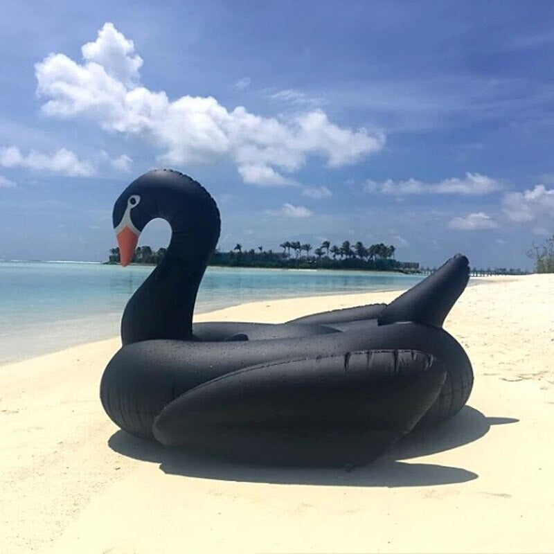 A giant black swan pool float resting on a sandy beach on a sunny day.