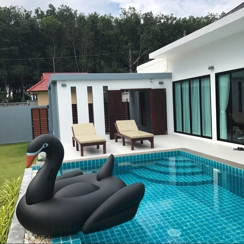 A huge black swan pool float in a pool with a white house in the background.