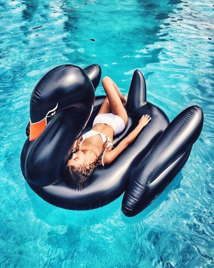 A woman sleeping and relaxing on a black swan pool float in a pool.