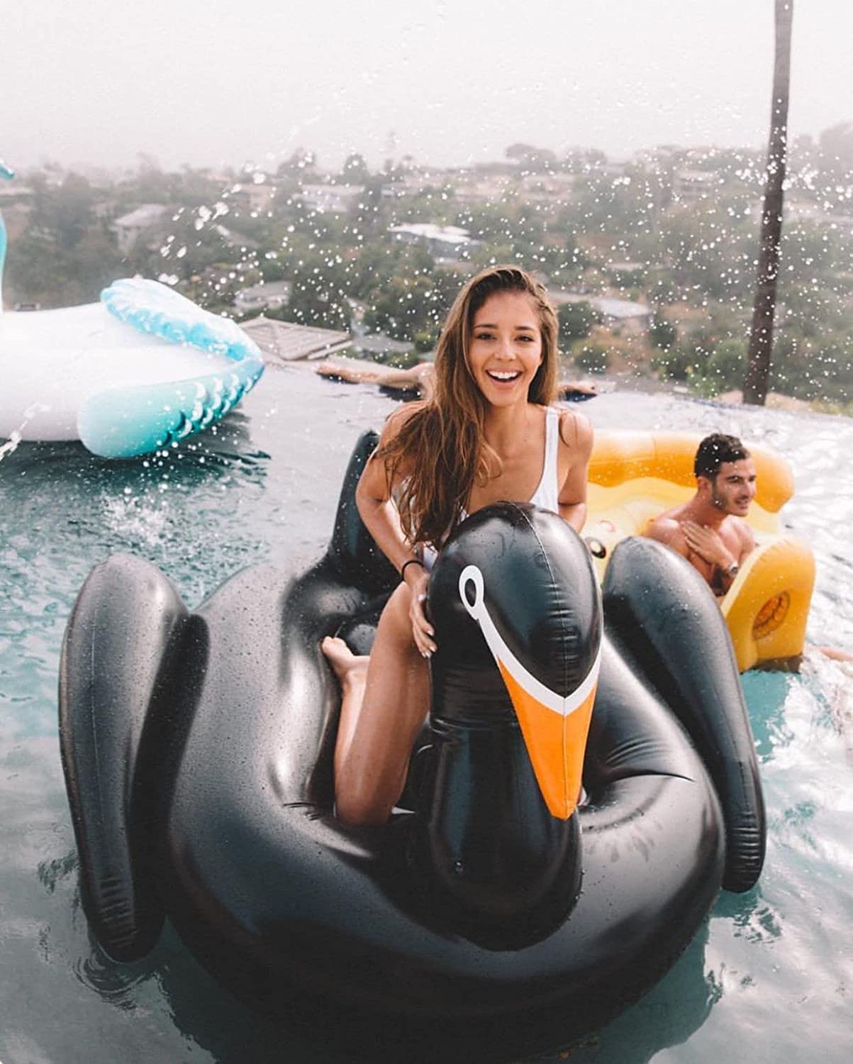 A smiling woman sitting in a black swan pool float while in a pool.
