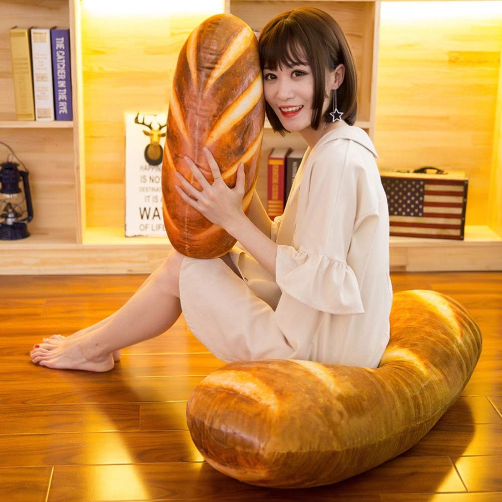 A woman sitting on a giant bread pillow and she is also holding a giant bread pillow while smiling