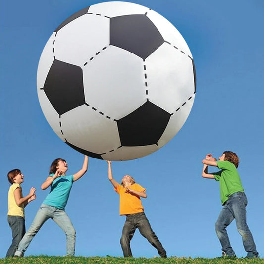 A giant inflatable soccer ball being tossed in the air by four kids who are standing on a green lawn with a clear blue sky behind them.