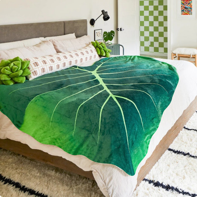 A giant blanket shaped like a giant green leaf spread out on a bed.
