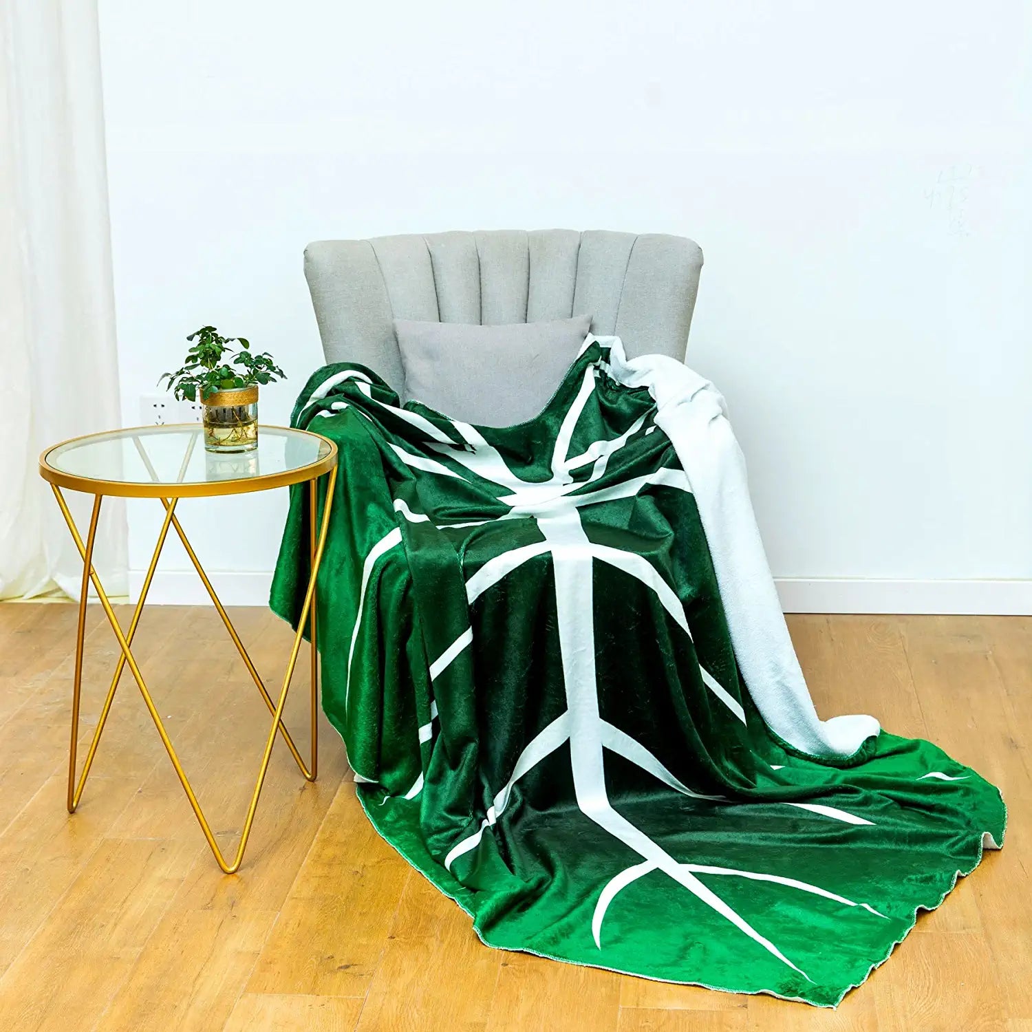 A green and white blanket shaped like a giant leaf draped over a grey chair.