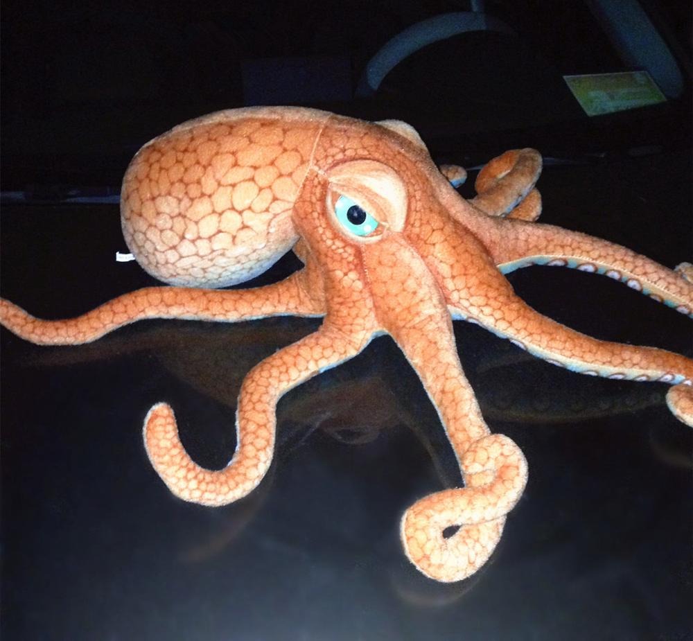 A octopus plush toy sitting on the hood of a car.