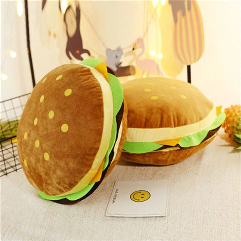 Two large pillows shaped like hamburgers which include plush cheese, patty and lettuce.