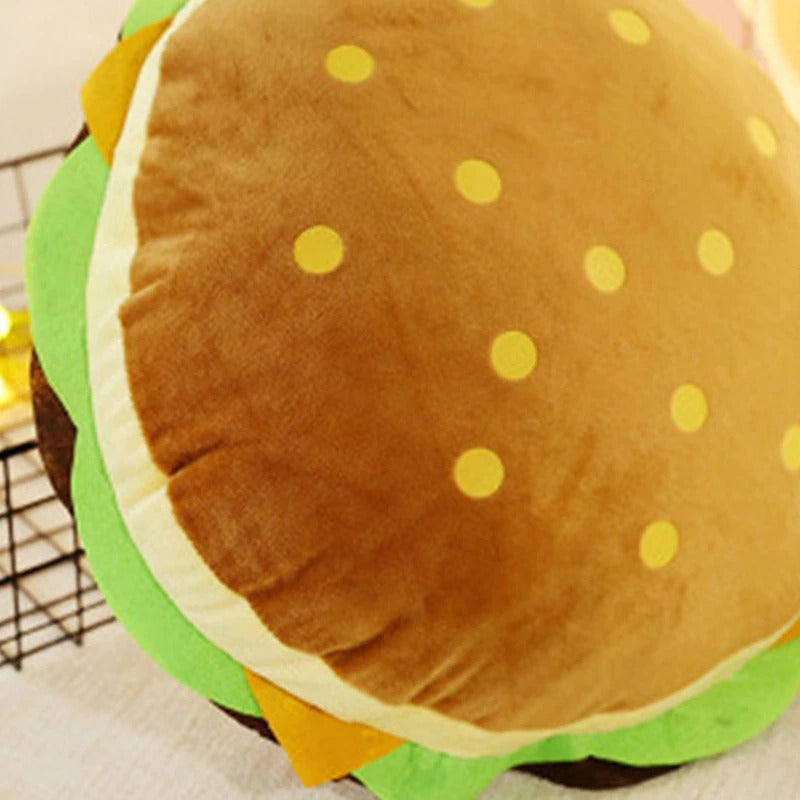 A close up view of a large hamburger shaped pillow with a sesame bun, cheese, lettuce and patty.