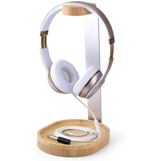 A pair of white headphones on a wooden and alloy headphone stand. The stand also features a cable-tidy to store the cable of the headphones beneath it.