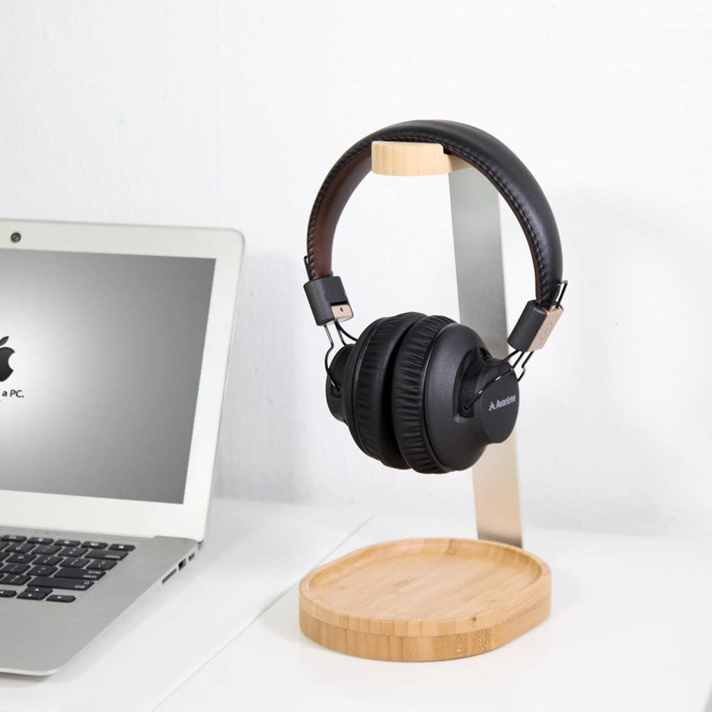 A black pair of headphones on a wooden and metal headphone stand. There is a laptop computer next to the stand.