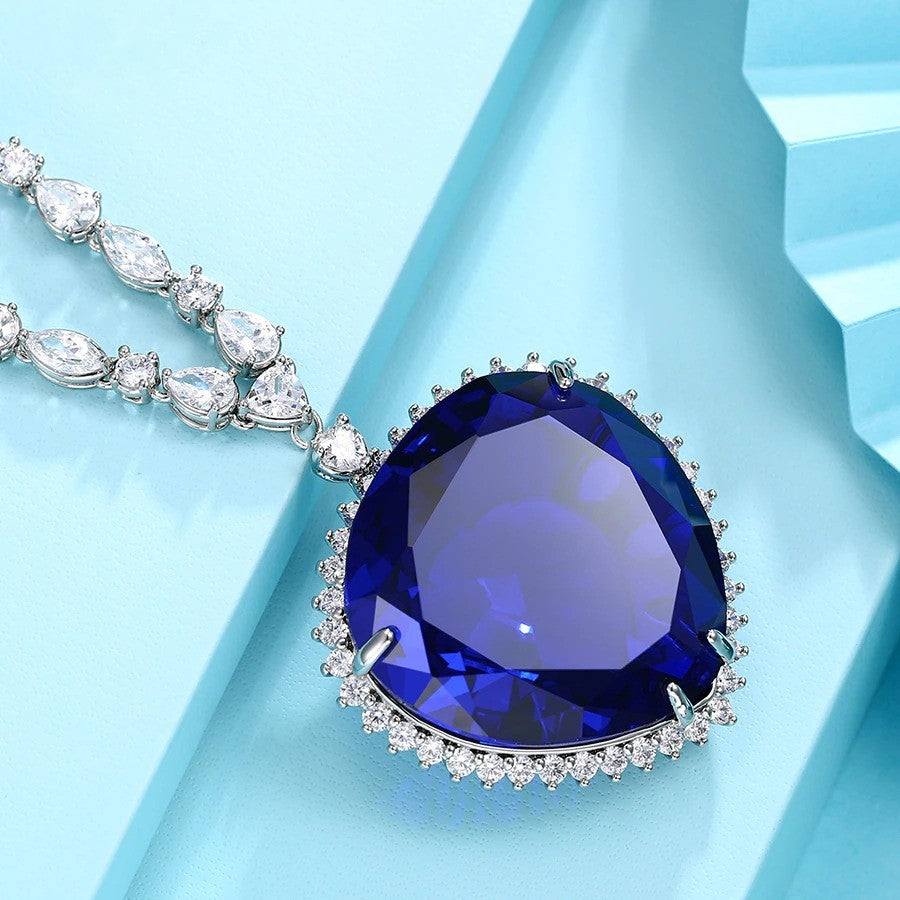 A replica of the Heart of the Ocean necklace from Titanic. This necklace is a close up of the pendant and some links from the chain can be seen. This is on a sky-blue coloured background.