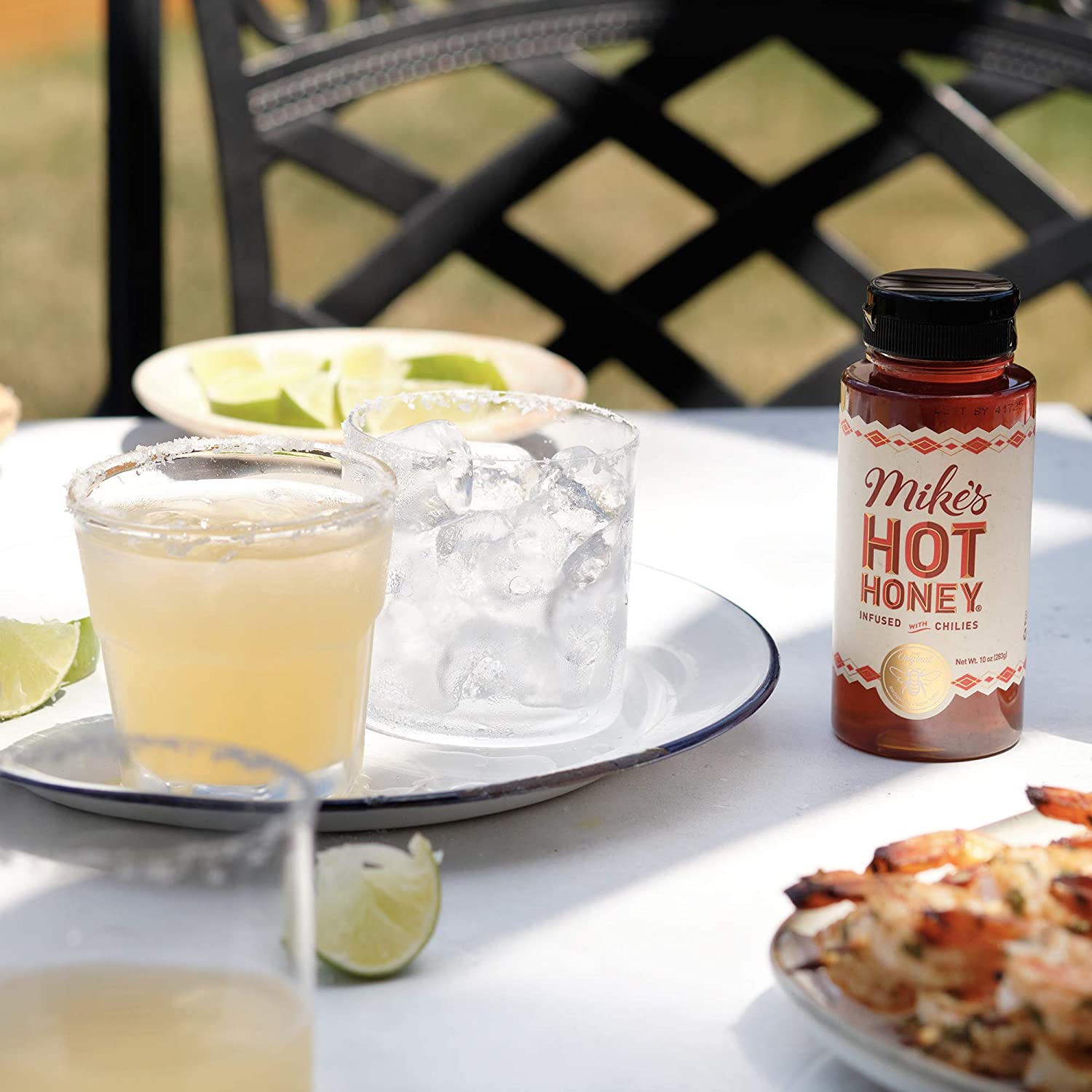 A jar of Mike's hot honey is on a table next to a plate which has two cocktails on it.