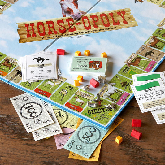 A close up section of the board piece from the game called Horse-opoly. There is fake cash, cards, tokens and small barns.