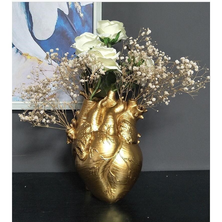 A gold colored human heart shaped vase complete with arteries. The holes of the arteries are filled with white roses and white baby’s breath flowers. 