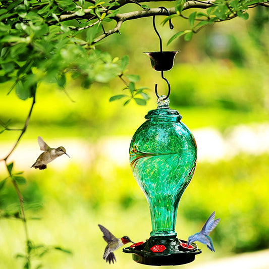 A hummingbird feeder is hanging from a tree outdoors with 3 hummingbirds around it.