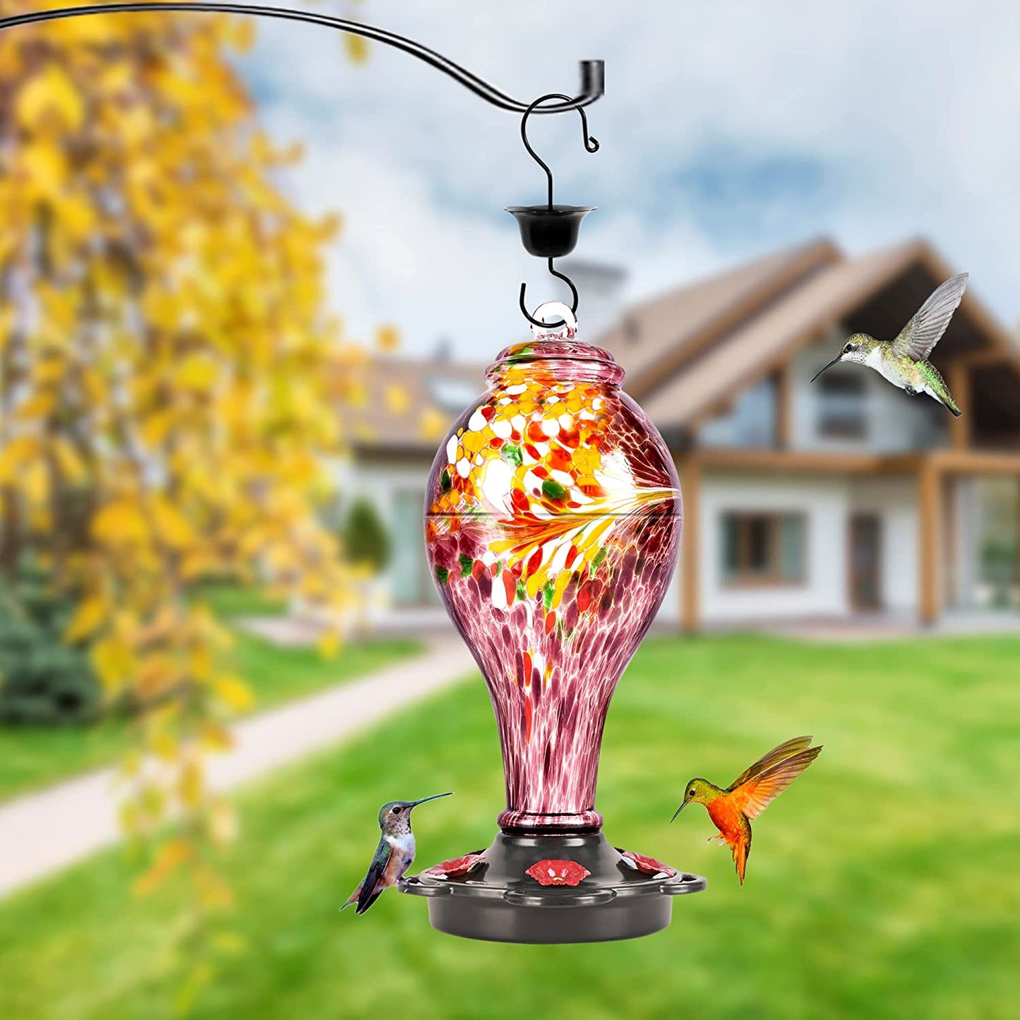 A purple colored hummingbird feeder is hanging up outdoors with 3 hummingbirds flying around it.