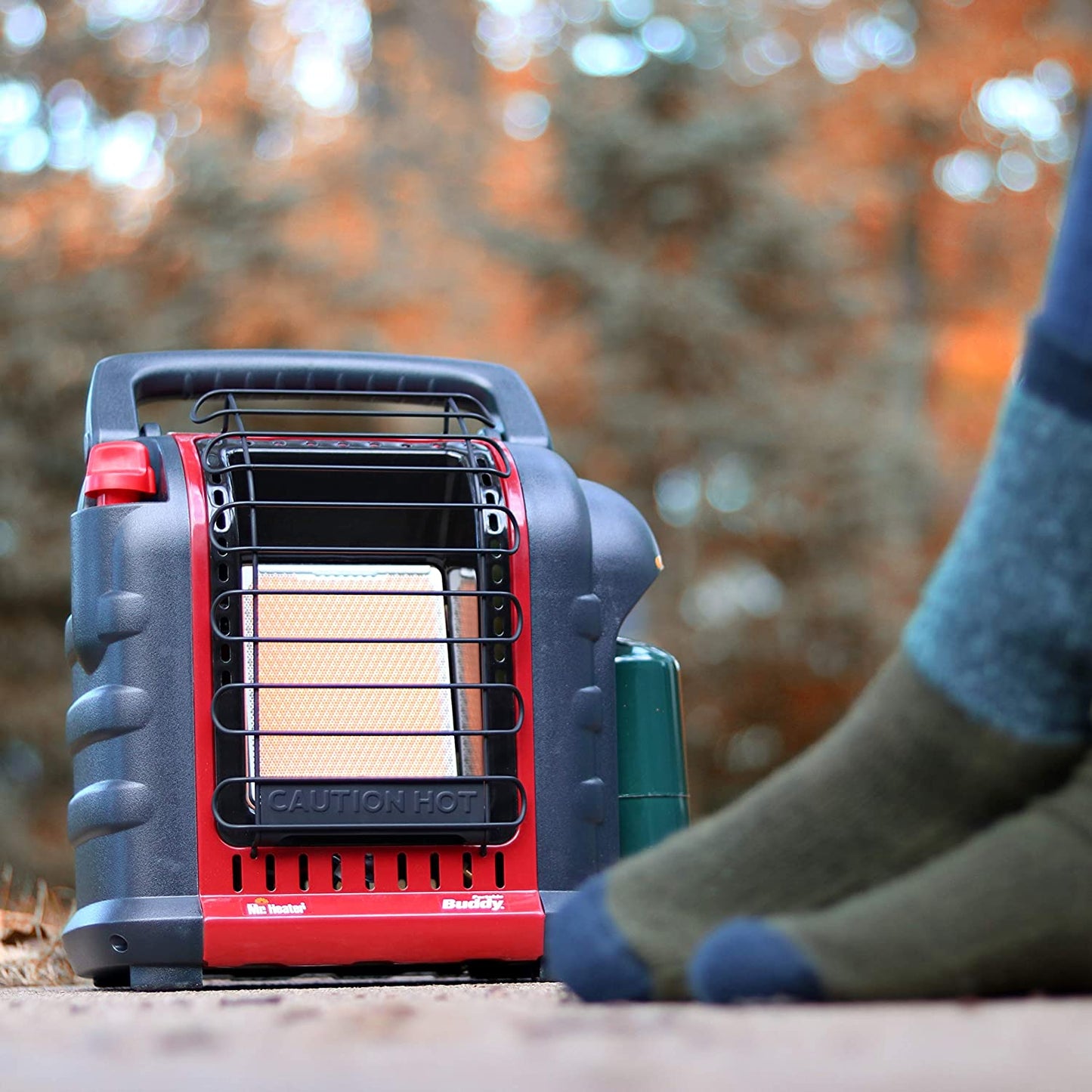 An indoor outdoor propane heater being used outdoors with a persons warming their feet near the heater.