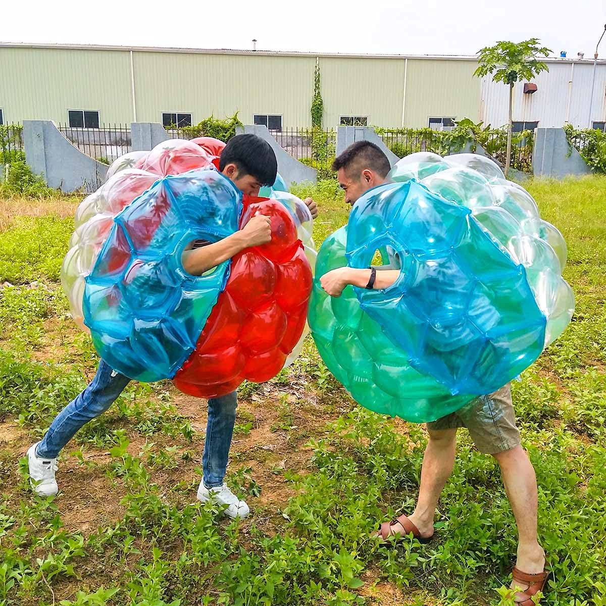 2 adults outdoors wearing giant inflatable bubble balls bumping into each other.