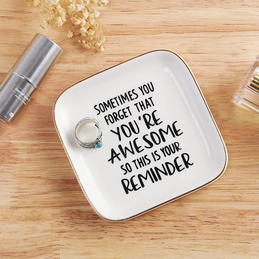 A stylish white ring dish with a printed quote which says, "Sometimes you forget that you're awesome, so this is your reminder"