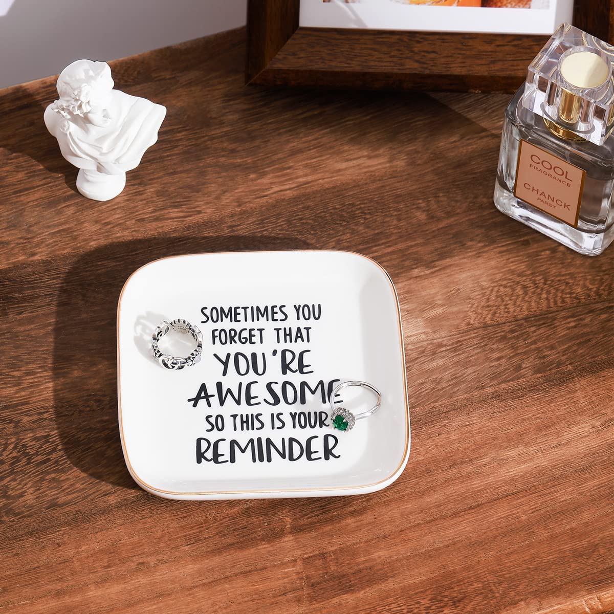 A ring trinket dish on a dark wooden table. A quote is printed on the dish which says, "Sometimes you forget that you're awesome, so this is your reminder".