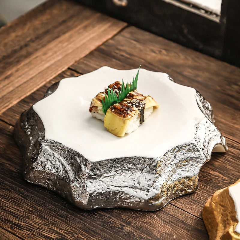 An irregular shaped silver ceramic dinner plate. The plate has silver colored sides and a white ceramic top. The plate has two pieces of sushi on it.