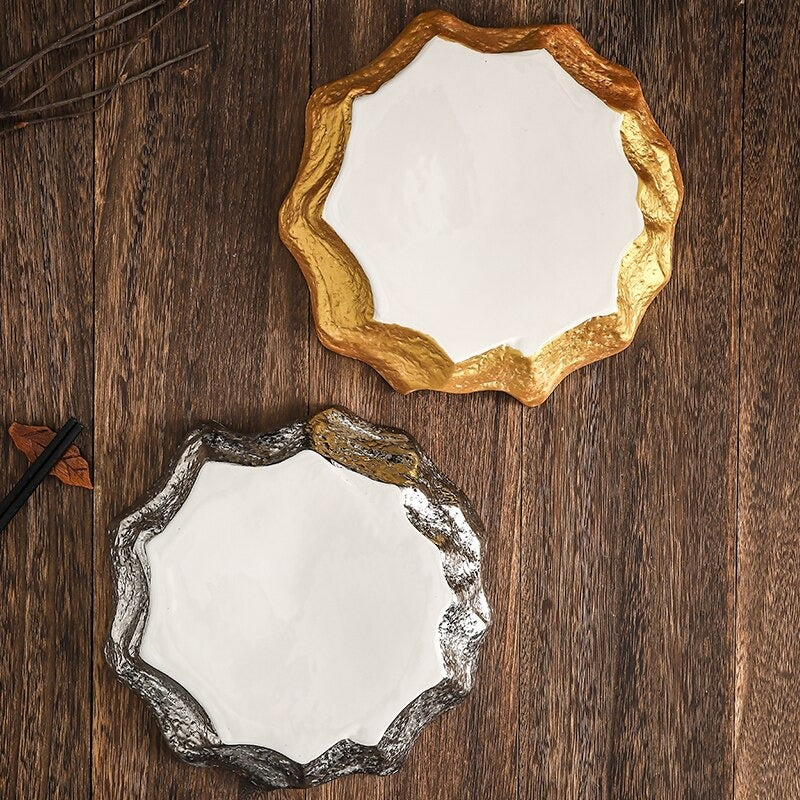 Aerial view of two irregular shaped ceramic dinner plates. One has gold sides and the other silver sides. The plates are on a wooden table.