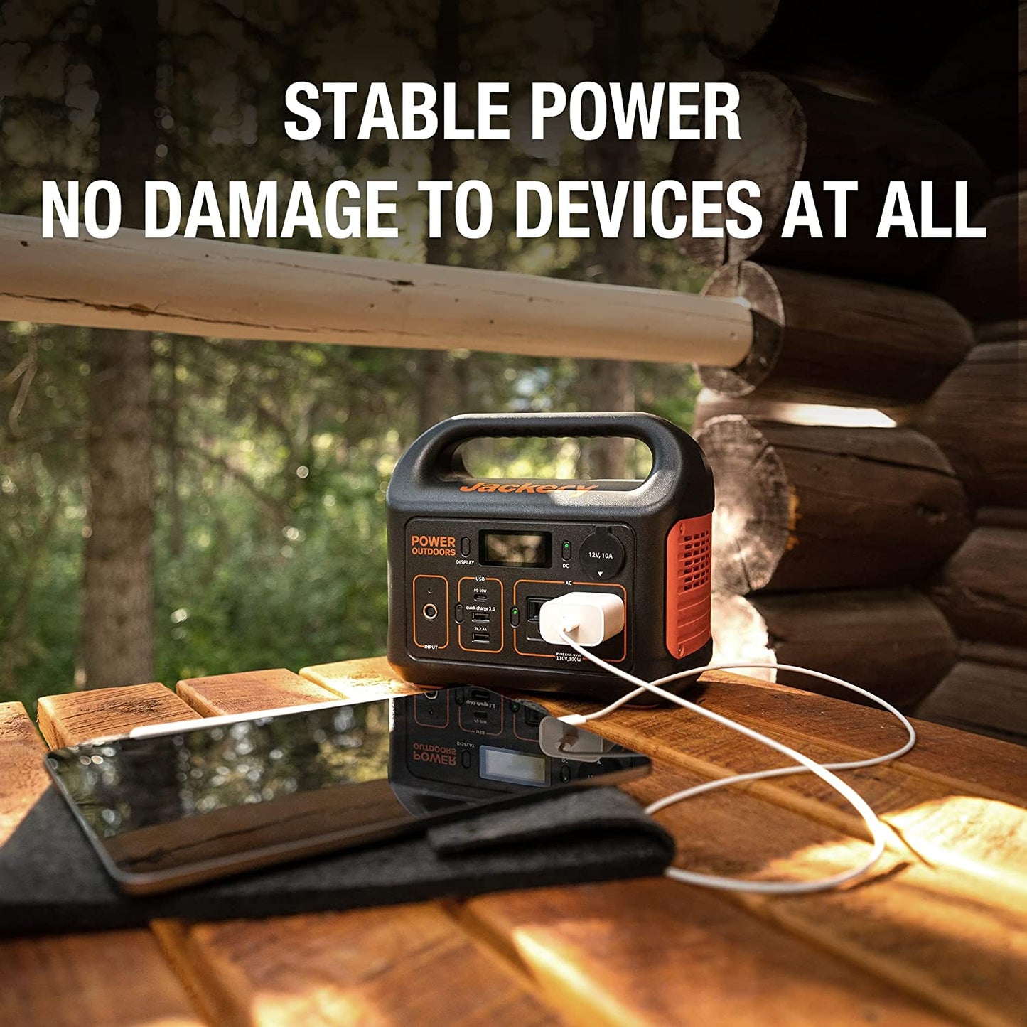 A Jackery portable power station is outdoors with an ipad plugged in getting charged up. The text reads, 'Stable power, no damage to devices at all.'