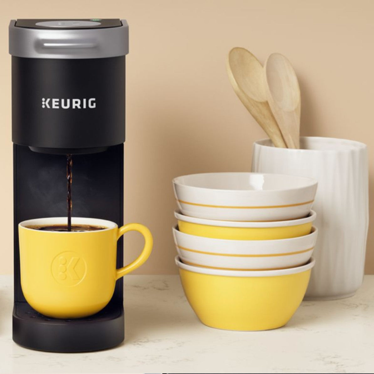 A black colored Keurig K-Mini coffee machine in a kitchen next to bowls and wooden spoons.