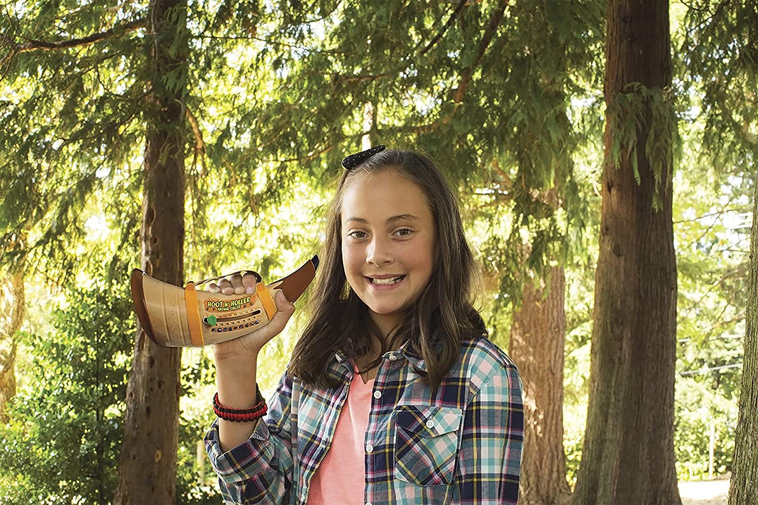 A girl is outdoors smiling and holding a hoot n holler animal caller toy.
